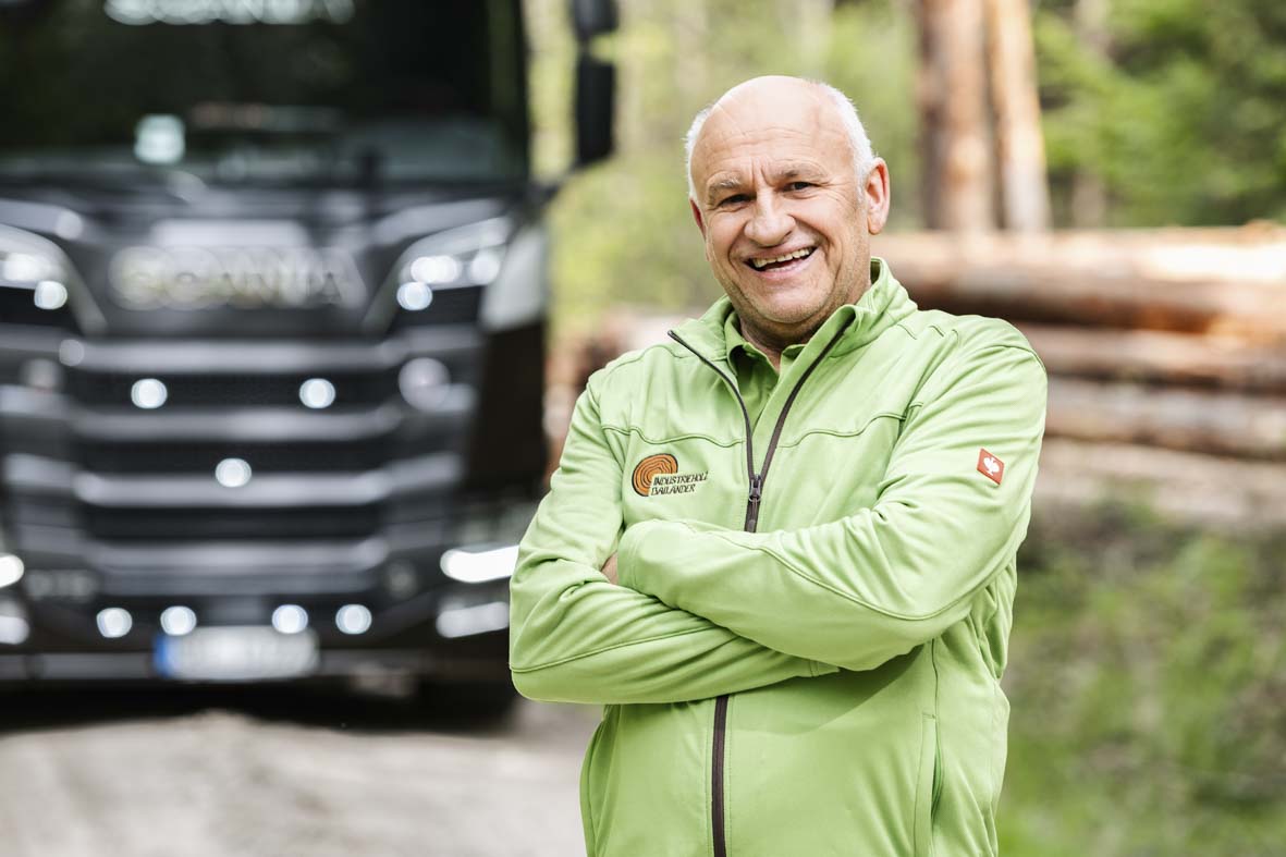 Portraitaufnahme im Wald von Dieter Bailänder. Im Hintergrund ein LKW und ein Stapel Baumstämme in der Unschärfe.